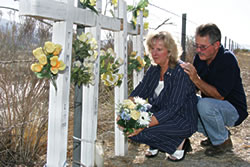 Alice and Tom Renolds kneel beside the crosses Tom made by hand; each symbolizes one of the lives lost on February 17, 2000.
