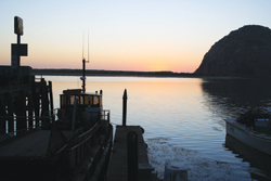 The setting sun highlights Morro Rock and a commercial fishing boat tied up at Morro Bay.